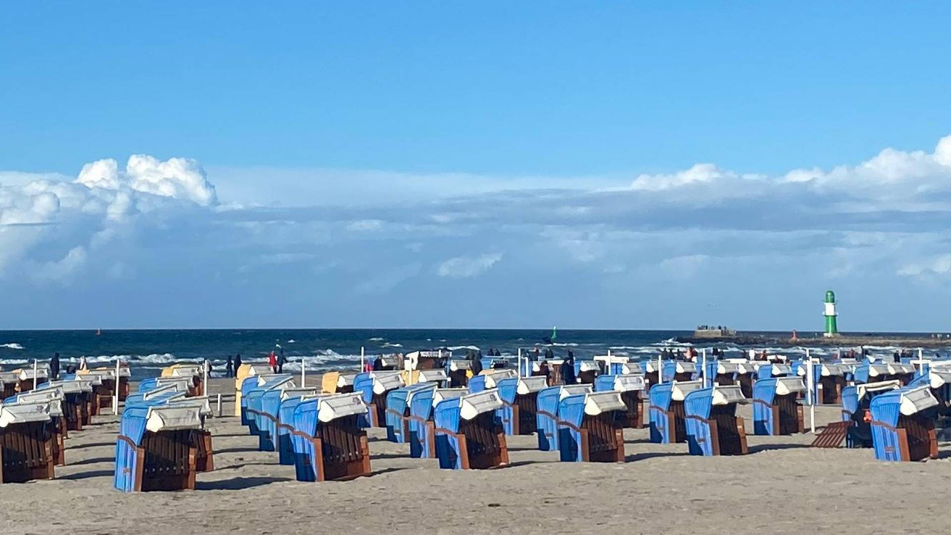 Ostseestrand voll mit Strandkörben und im Hintergrund ist der Grüne Leuchtturm
